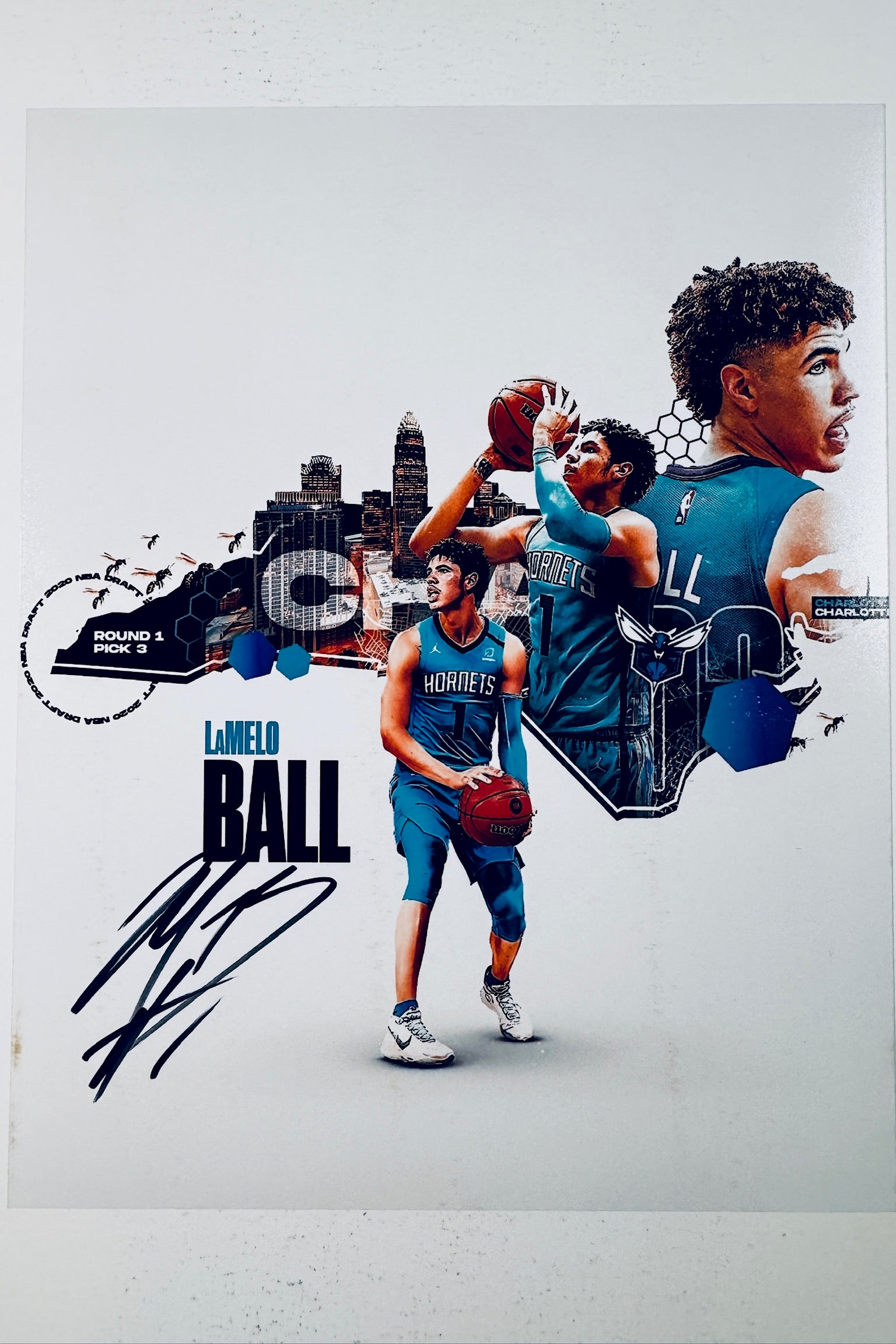 Signed 8x10 matte sports collage photo of LaMelo Ball in his blue Charlotte Hornets uniform holding a basketball, featuring graphics of the Charlotte skyline and a black ink autograph across the lower-left area.