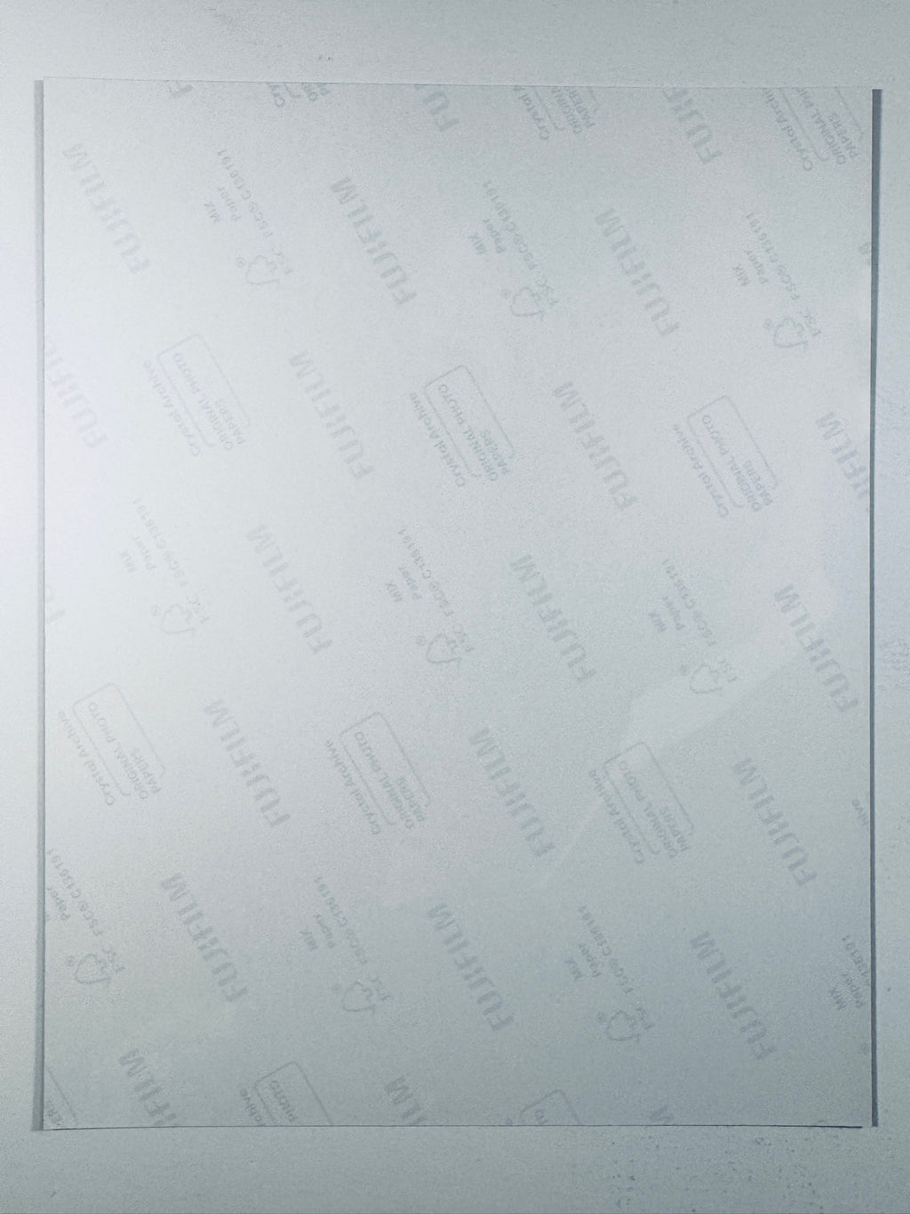 The plain white reverse side of a photographic print showing faint translucent watermark patterns and repeating Fujifilm paper logos.