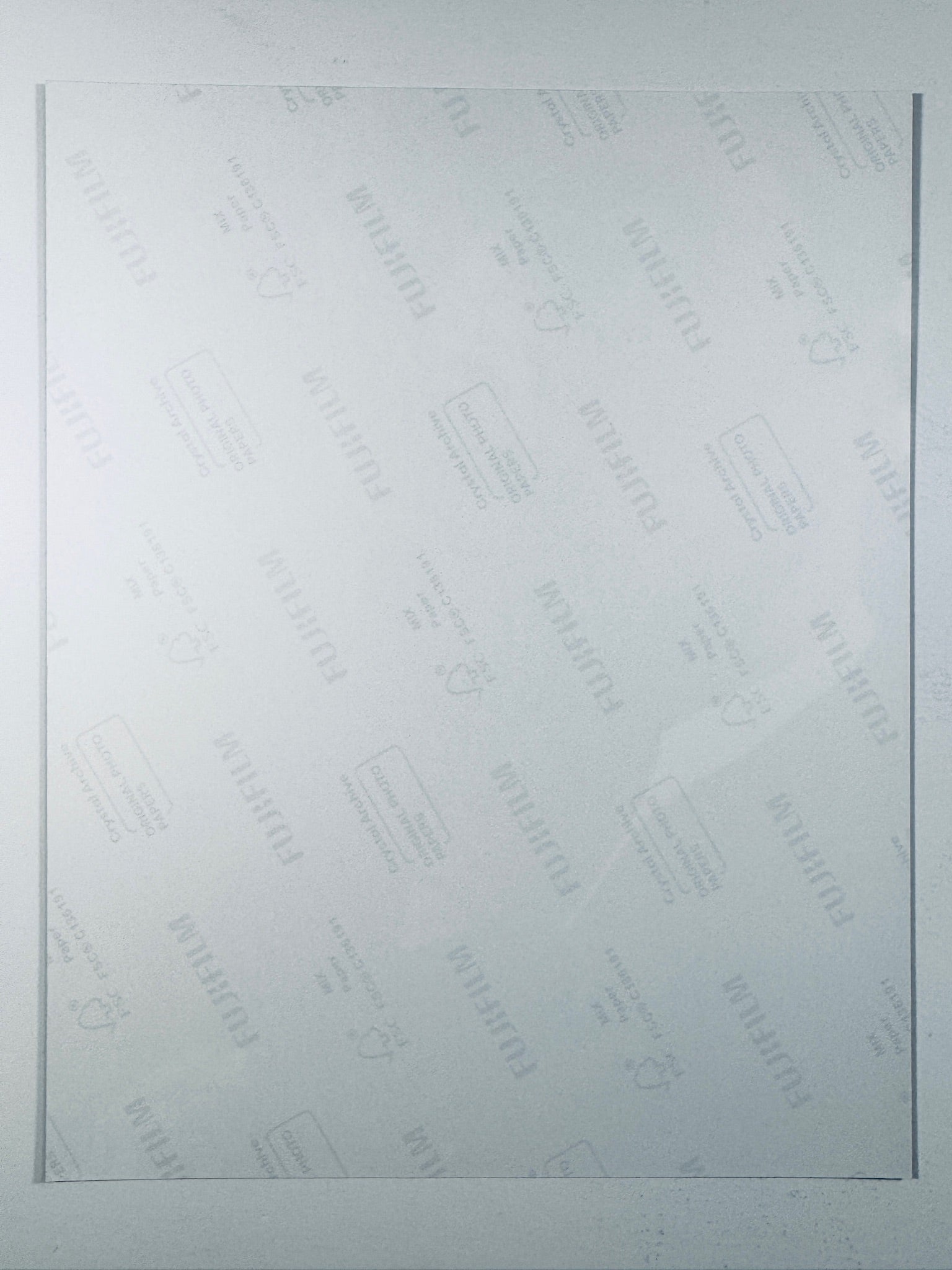 The plain white reverse side of a photographic print showing faint translucent watermark patterns and repeating Fujifilm paper logos.