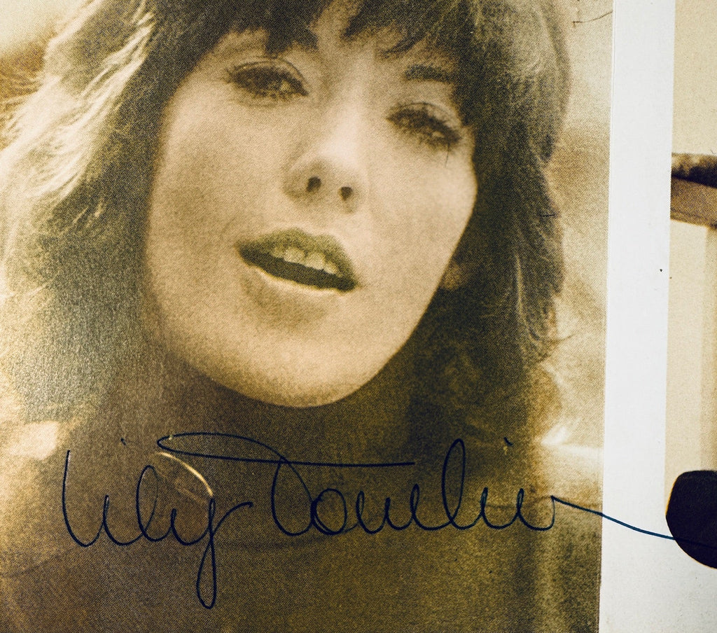 Close-up of Lily Tomlin's handwritten signature in pen on a vintage promotional card.
