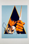 A portrait of Malcolm McDowell as Alex DeLarge from A Clockwork Orange, holding a knife and featuring a signature in black ink on the lower left.