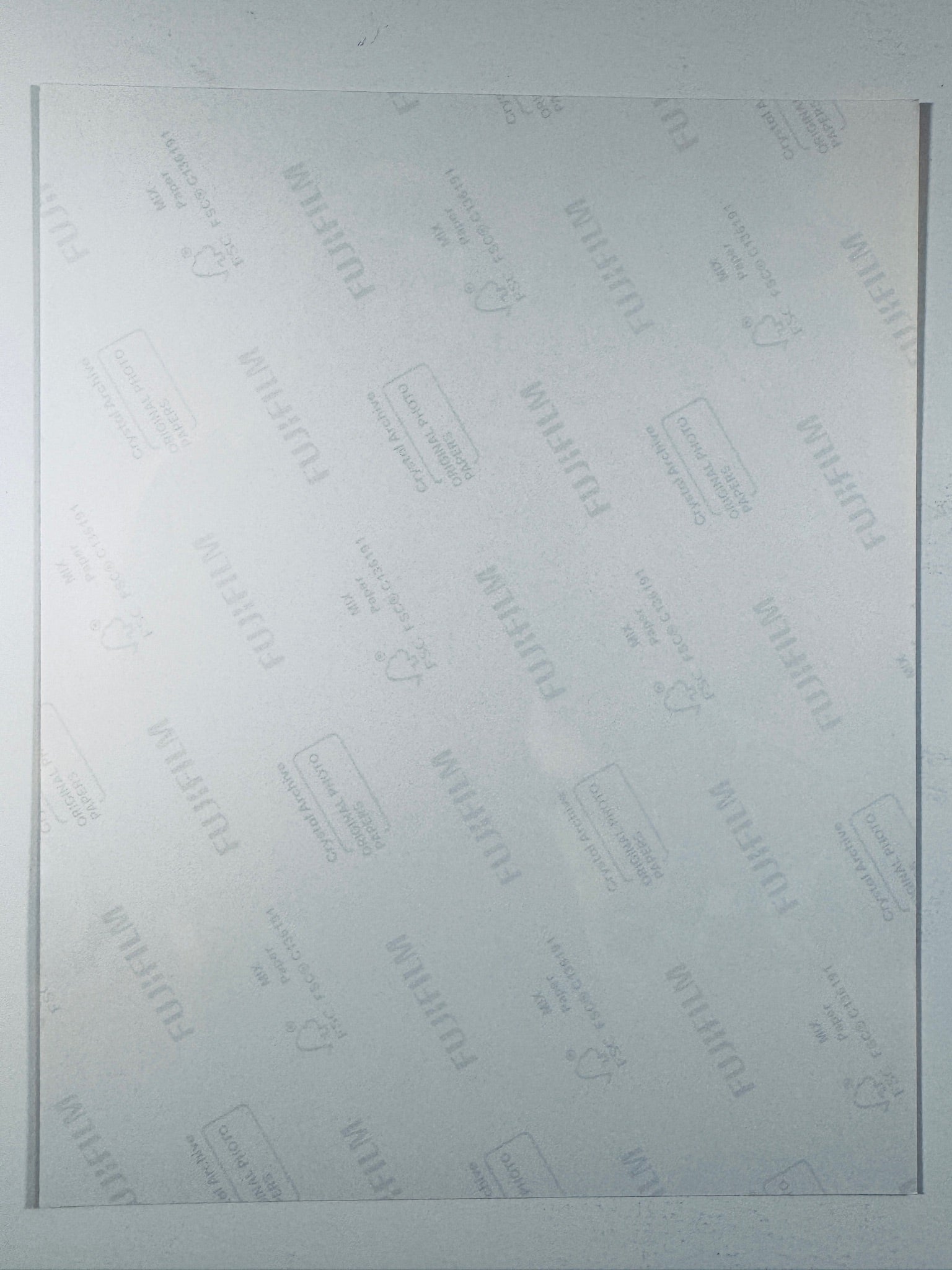 The plain white reverse side of a photographic print showing faint translucent watermark patterns and repeating Fujifilm paper logos.