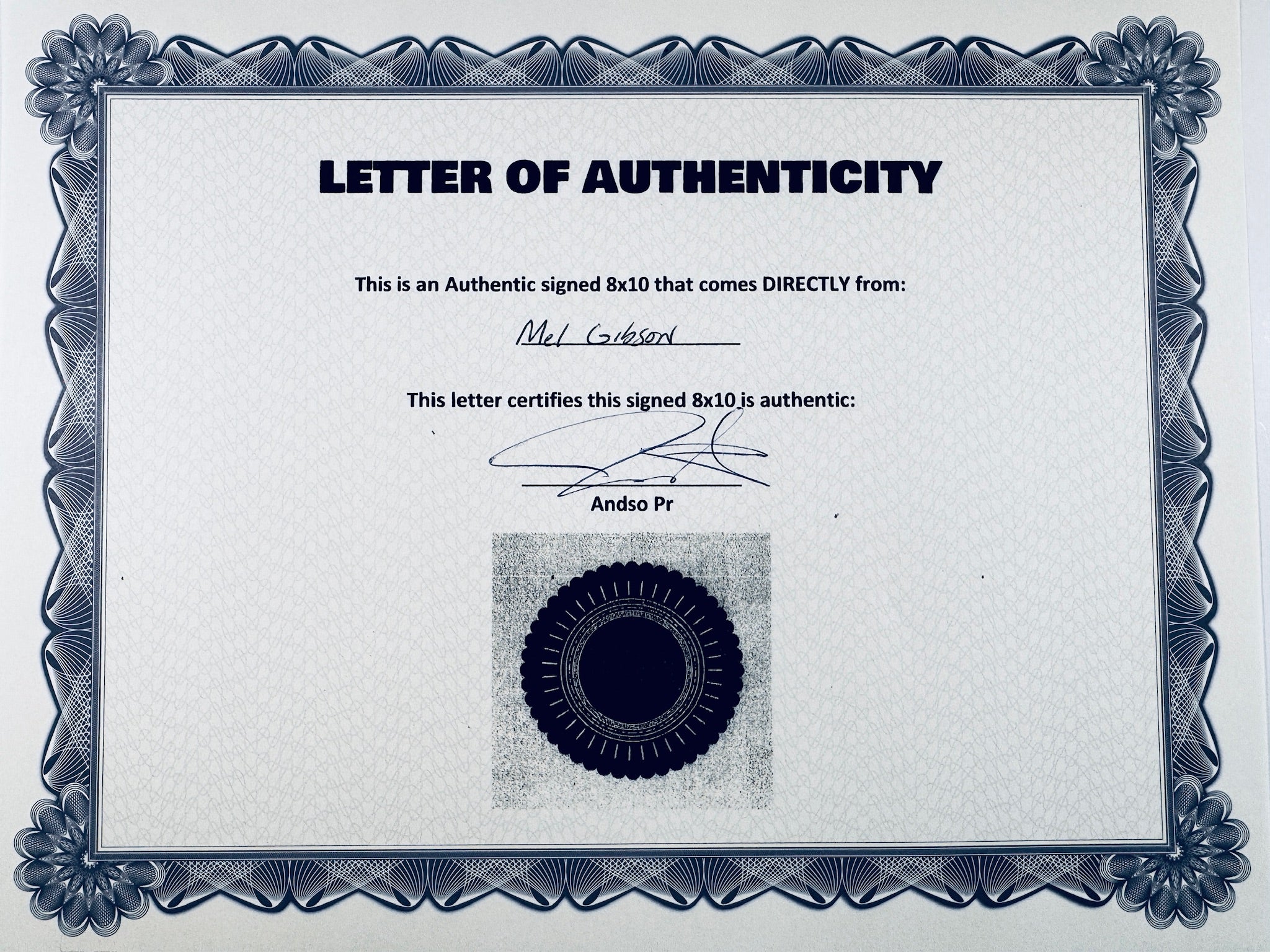A Certificate of Authenticity featuring a decorative blue-patterned border, text certifying an authentic signed 8x10 from Mel Gibson, a signature, and a dark circular seal graphic at the bottom center.