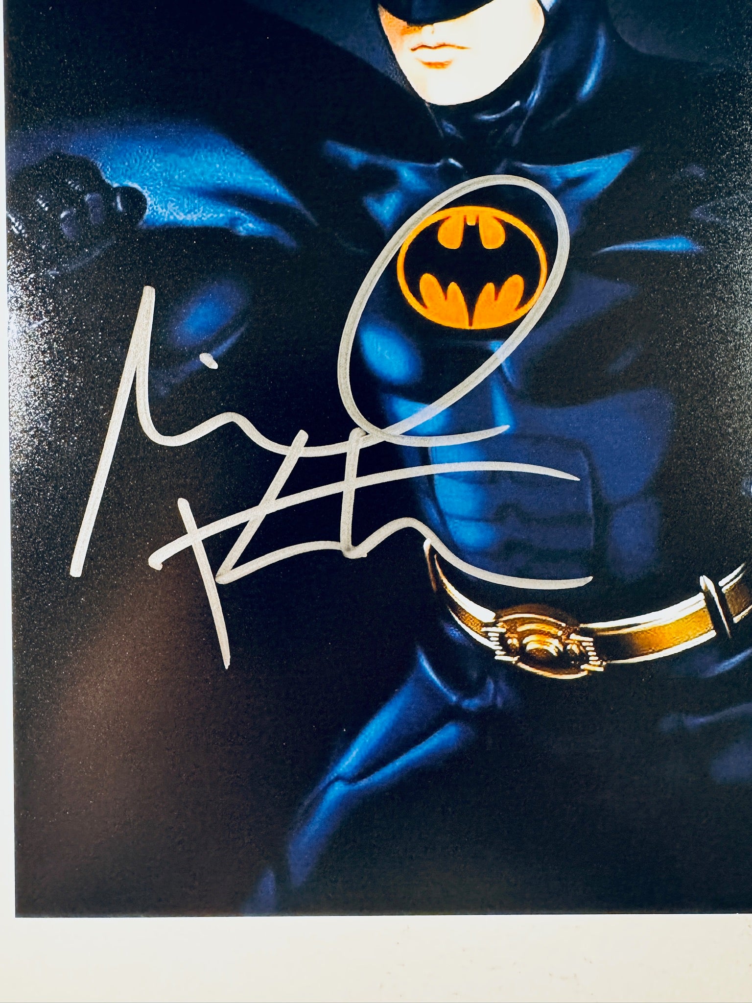 Close-up view of Michael Keaton's silver signature across the chest and emblem of the Batman promotional photograph.