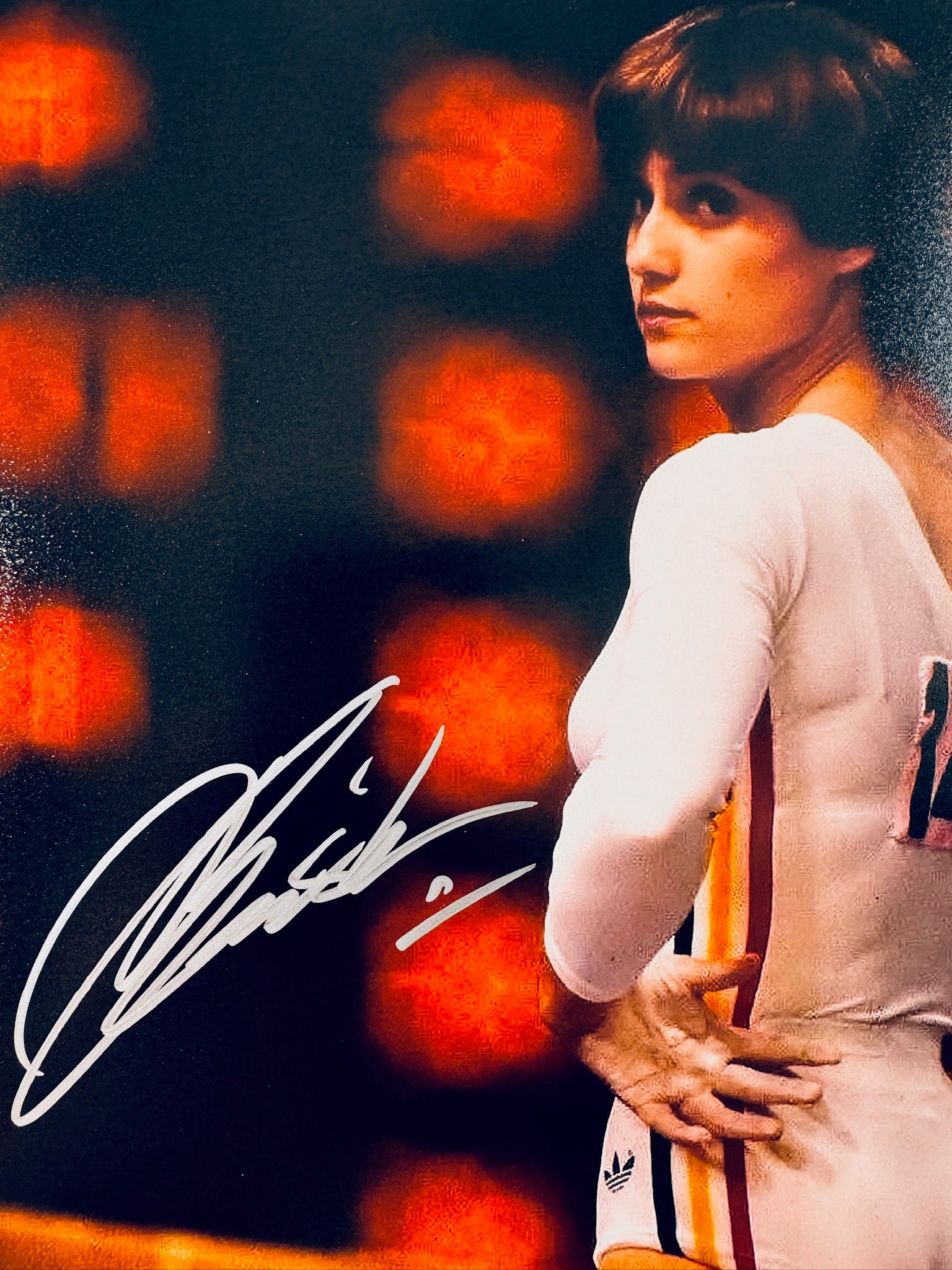 Close-up view of Nadia Comaneci's signature in metallic ink across the dark background of the promotional gymnast photo.