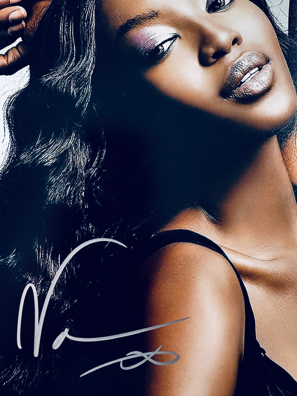 Close-up view of Naomi Campbell's signature in silver marker across the dark hair and background of the glamour portrait photo.
