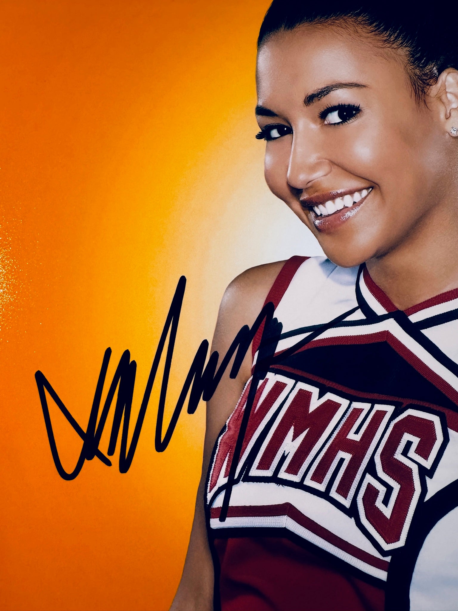 Close-up view of Naya Rivera's signature in black marker on her Glee cheerleader promotional photo.