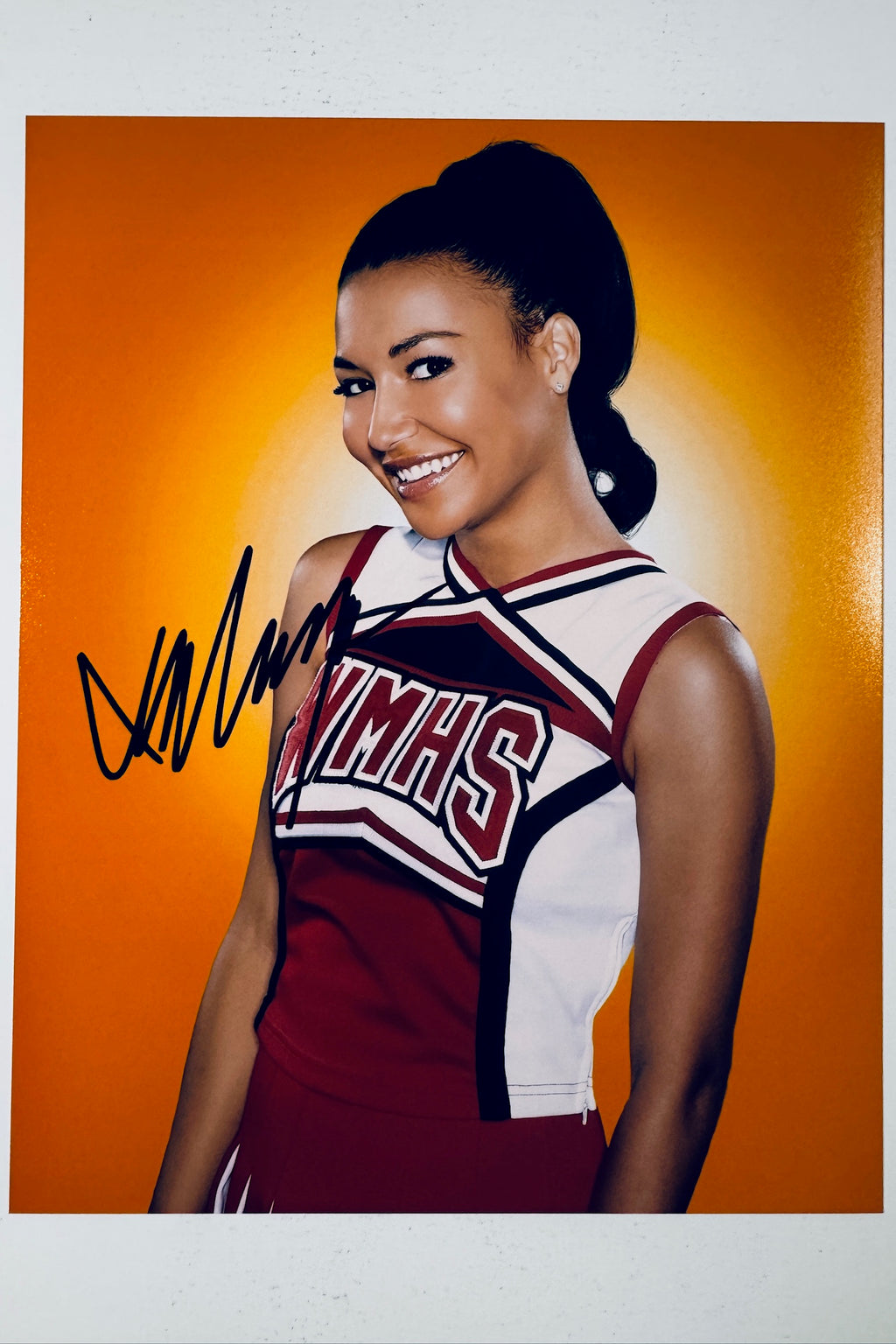 Signed 8x10 glossy photo of Naya Rivera as Santana Lopez in her McKinley High WMHS cheerleader uniform from Glee, featuring a bold black ink autograph.