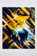 A dynamic action shot of Neymar in a yellow Brazil jersey set against a streaked dark and gold background, featuring a bold black marker signature across the center.
