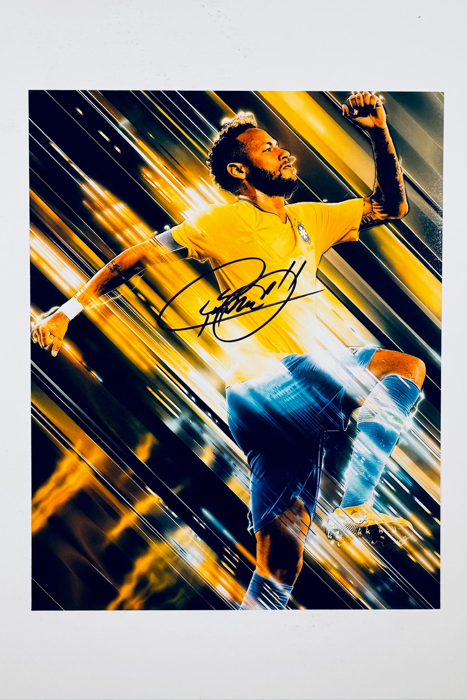 A dynamic action shot of Neymar in a yellow Brazil jersey set against a streaked dark and gold background, featuring a bold black marker signature across the center.