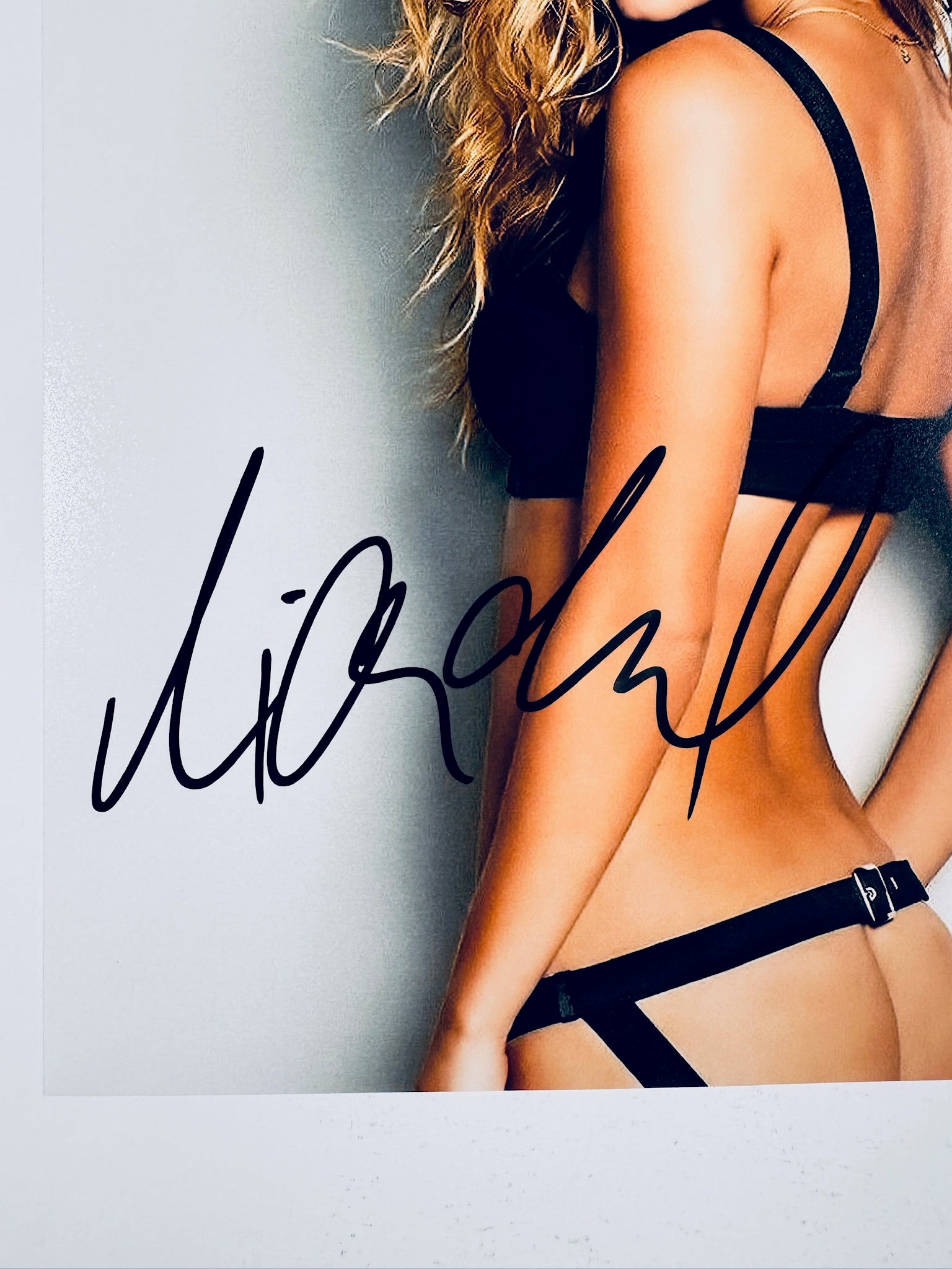 Close-up view of Nina Agdal's black autograph across her lower back and waist on the promotional photograph.