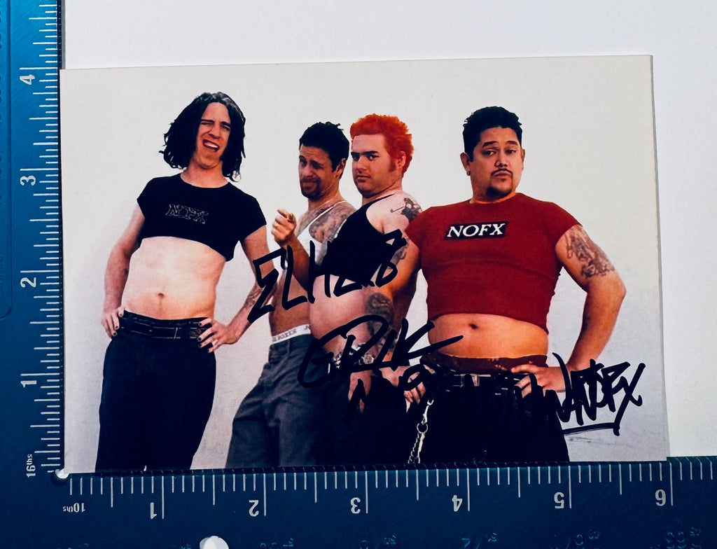 Autographed NOFX band photo placed against a measuring grid scale showing dimensions of 5 by 7 inches.