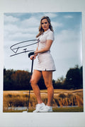Signed 8x10 matte photo of professional golfer Paige Spiranac standing on a golf course in a pink polo and skirt holding a club, featuring a bold black ink autograph.