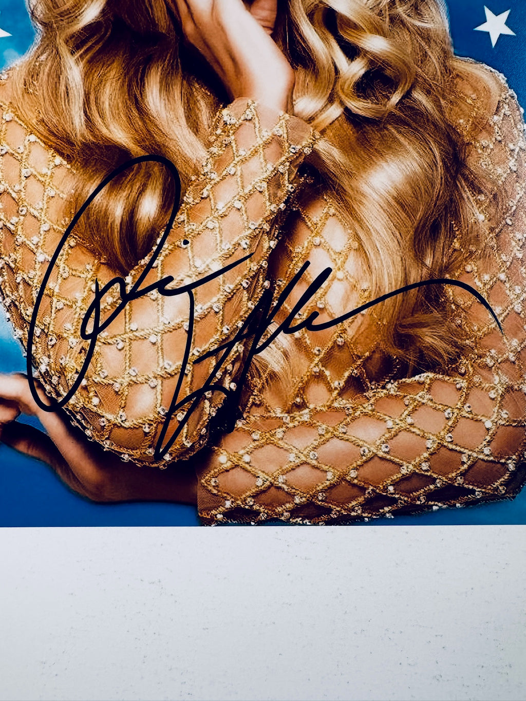 Close-up view of Paris Hilton's black signature across her sequined sleeve and torso on the promotional photograph.