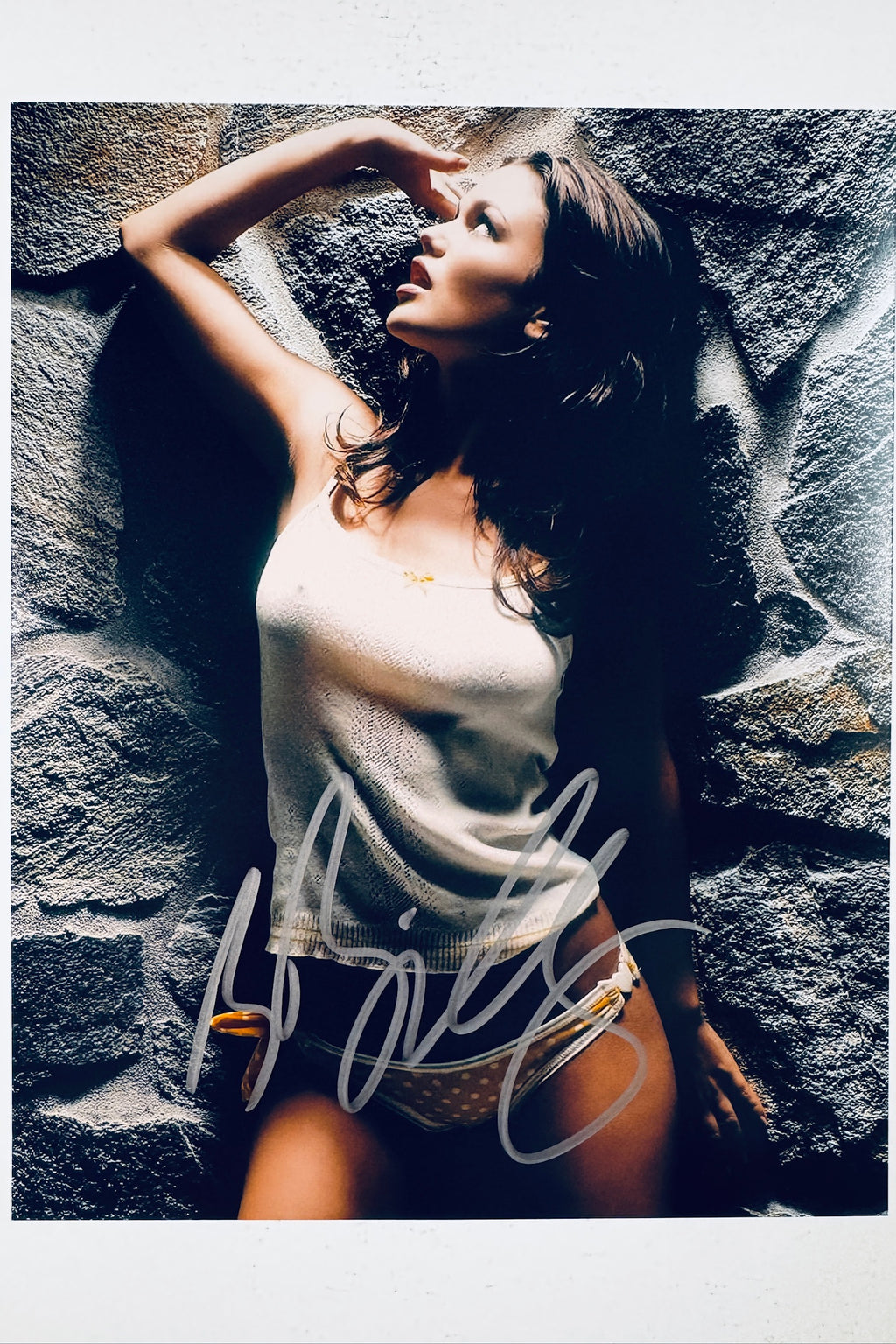 Signed full photo of Rachel Bilson posing against a stone wall wearing a white tank top and patterned bikini bottoms, featuring a silver autograph.