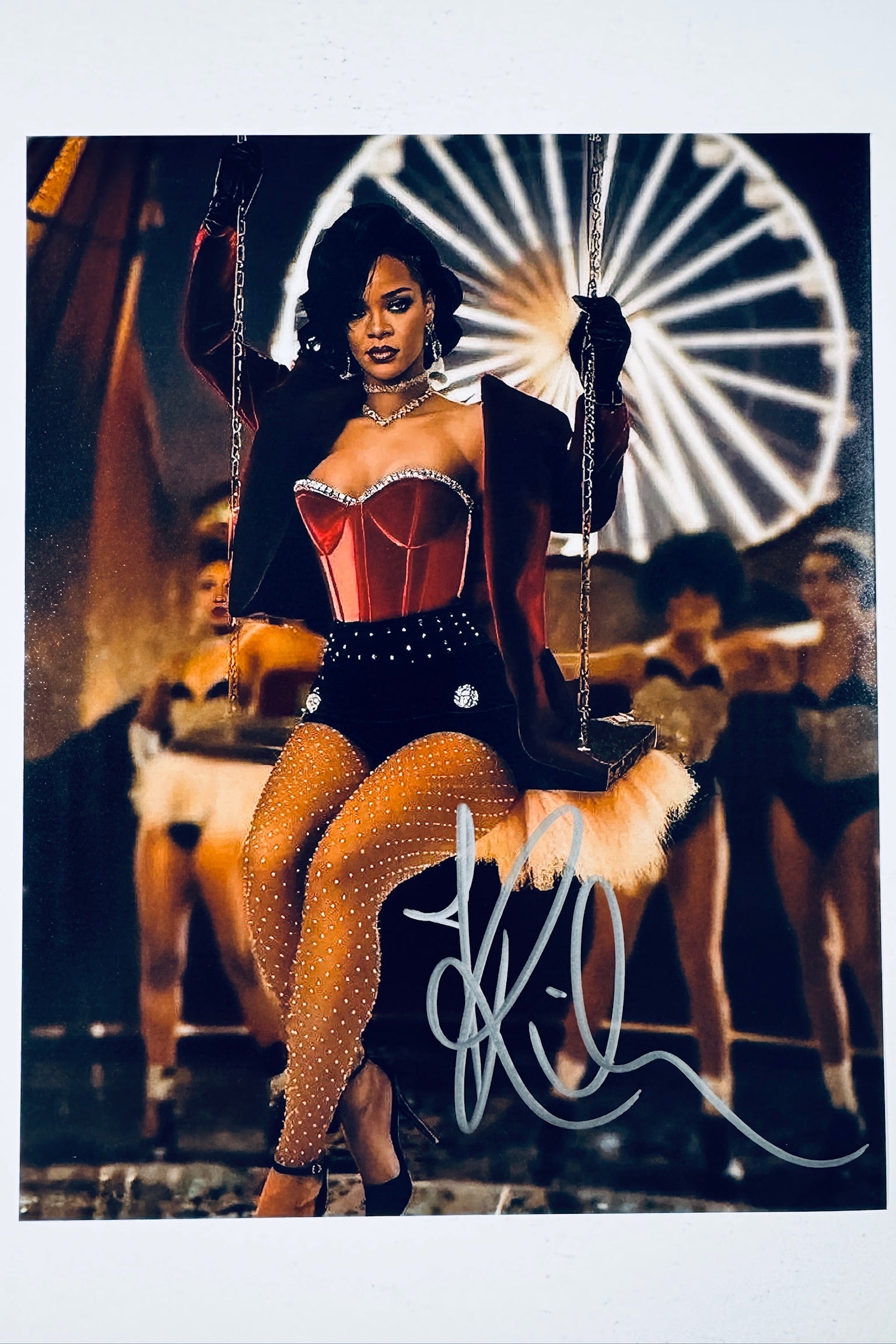 Rihanna hand-signed 8x10 matte photo posing on a swing in a red and black outfit with backup dancers and a ferris wheel in the background.