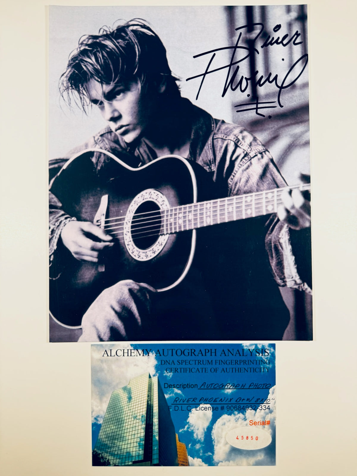 Autographed 8x10 black and white photo of River Phoenix playing an acoustic guitar with signature and Alchemy Autograph Analysis COA card.