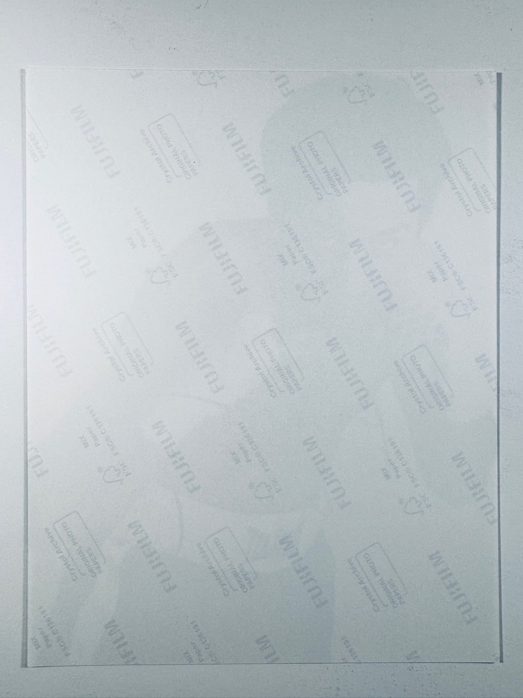 The plain white reverse side of a photographic print showing faint translucent watermark patterns and repeating Fujifilm paper logos.