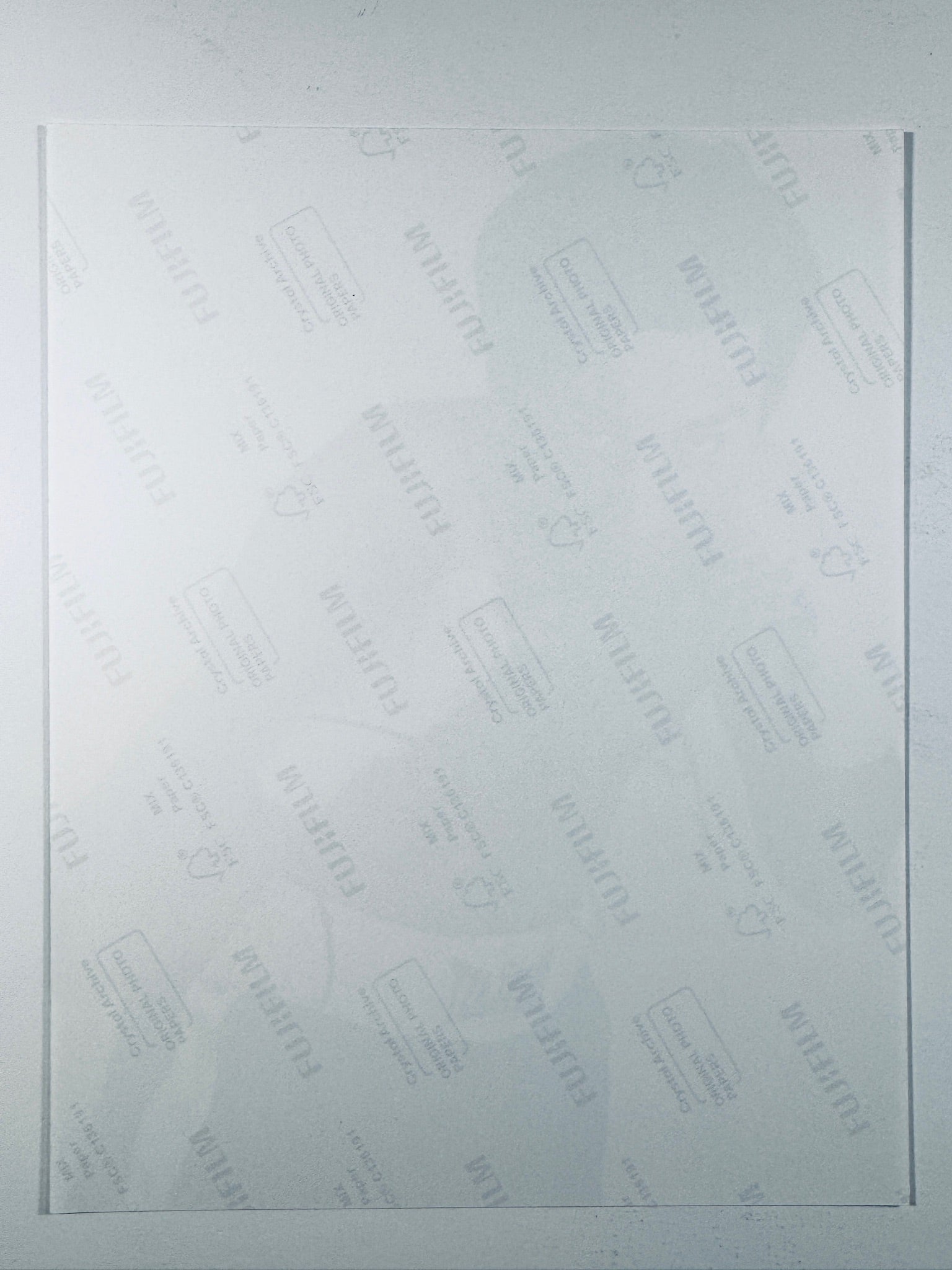 The plain white reverse side of a photographic print showing faint translucent watermark patterns and repeating Fujifilm paper logos.