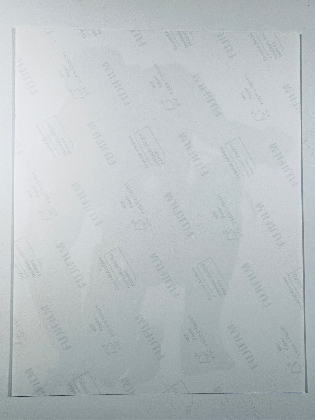 The plain white reverse side of a photographic print showing faint translucent watermark patterns and repeating Fujifilm paper logos.