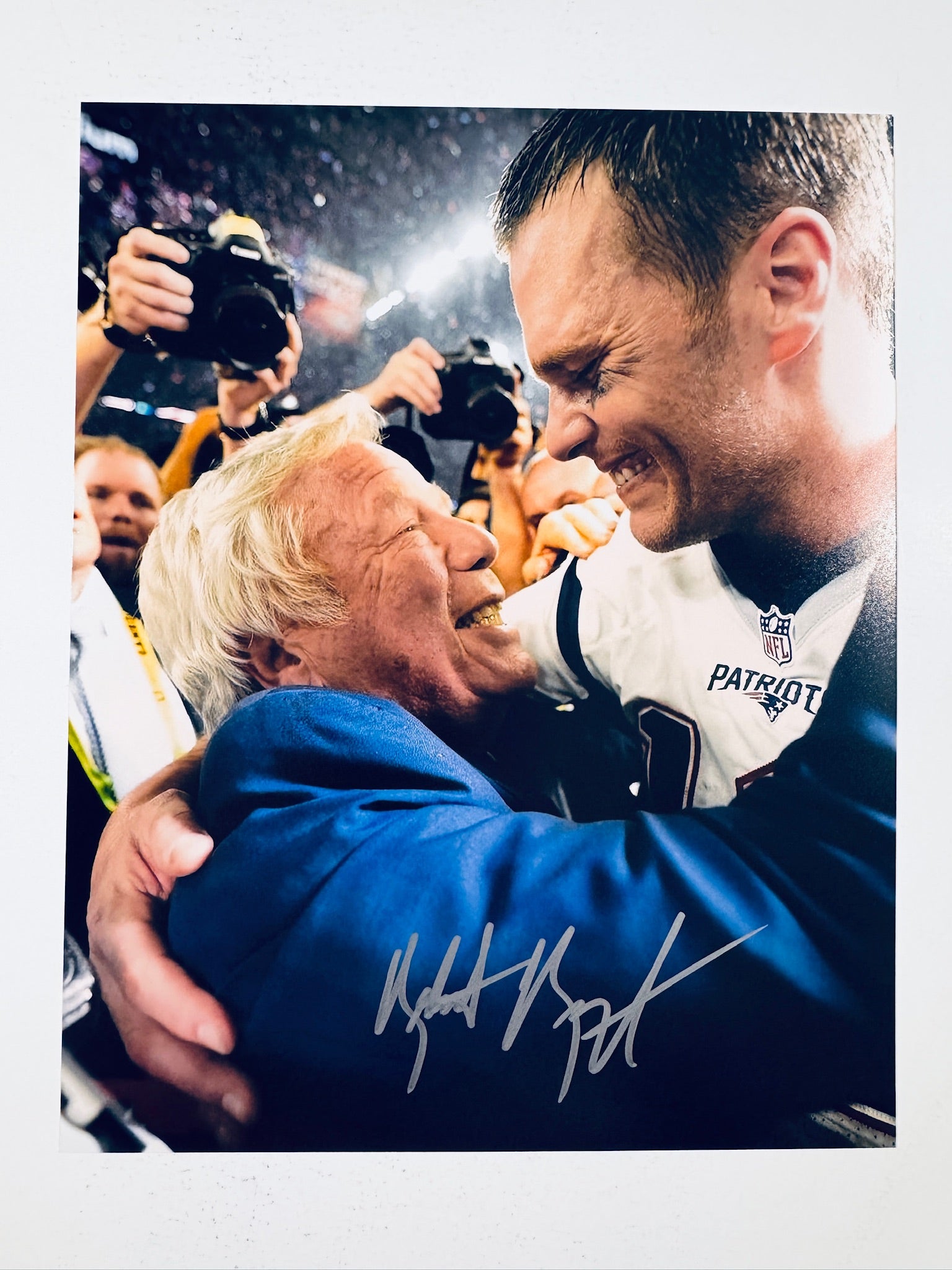 Signed 8x10 matte photo of New England Patriots owner Robert Kraft hugging quarterback Tom Brady in uniform, featuring a bold silver ink autograph by Robert Kraft across the lower section.