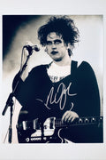 Alt Text: Signed 8x10 matte finish photo of Robert Smith of The Cure performing live with a microphone and guitar, featuring a bold silver ink autograph.