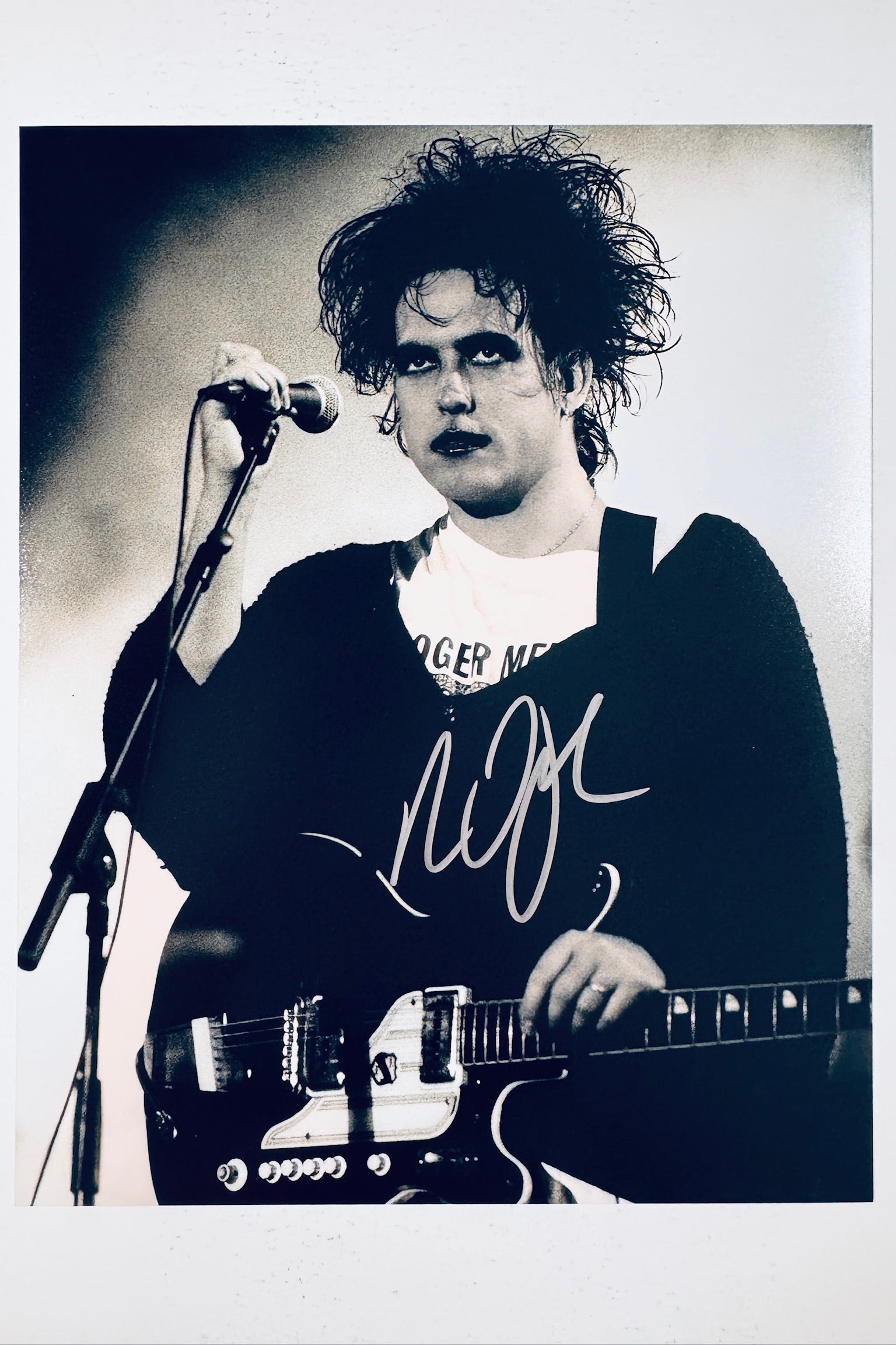 Alt Text: Signed 8x10 matte finish photo of Robert Smith of The Cure performing live with a microphone and guitar, featuring a bold silver ink autograph.