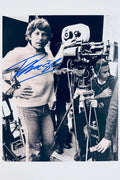 Autographed 8x10 black and white behind-the-scenes photo of director Roman Polanski next to a film camera, signed in blue ink.
