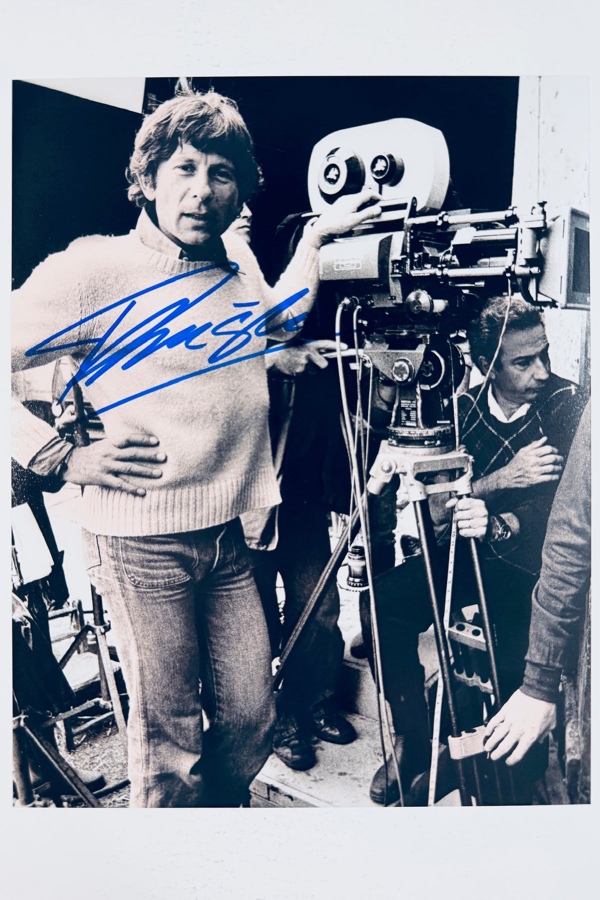 Autographed 8x10 black and white behind-the-scenes photo of director Roman Polanski next to a film camera, signed in blue ink.