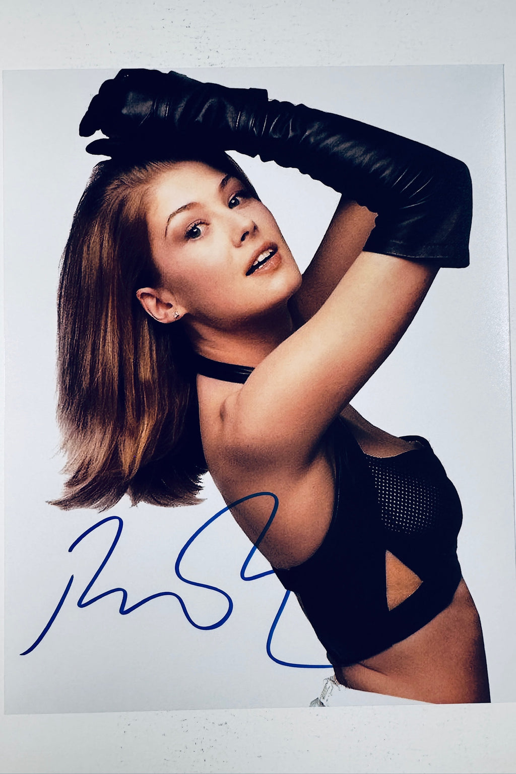 Signed 8x10 matte photo of Rosamund Pike posing in a black top with leather gloves, featuring a bold blue ink autograph.