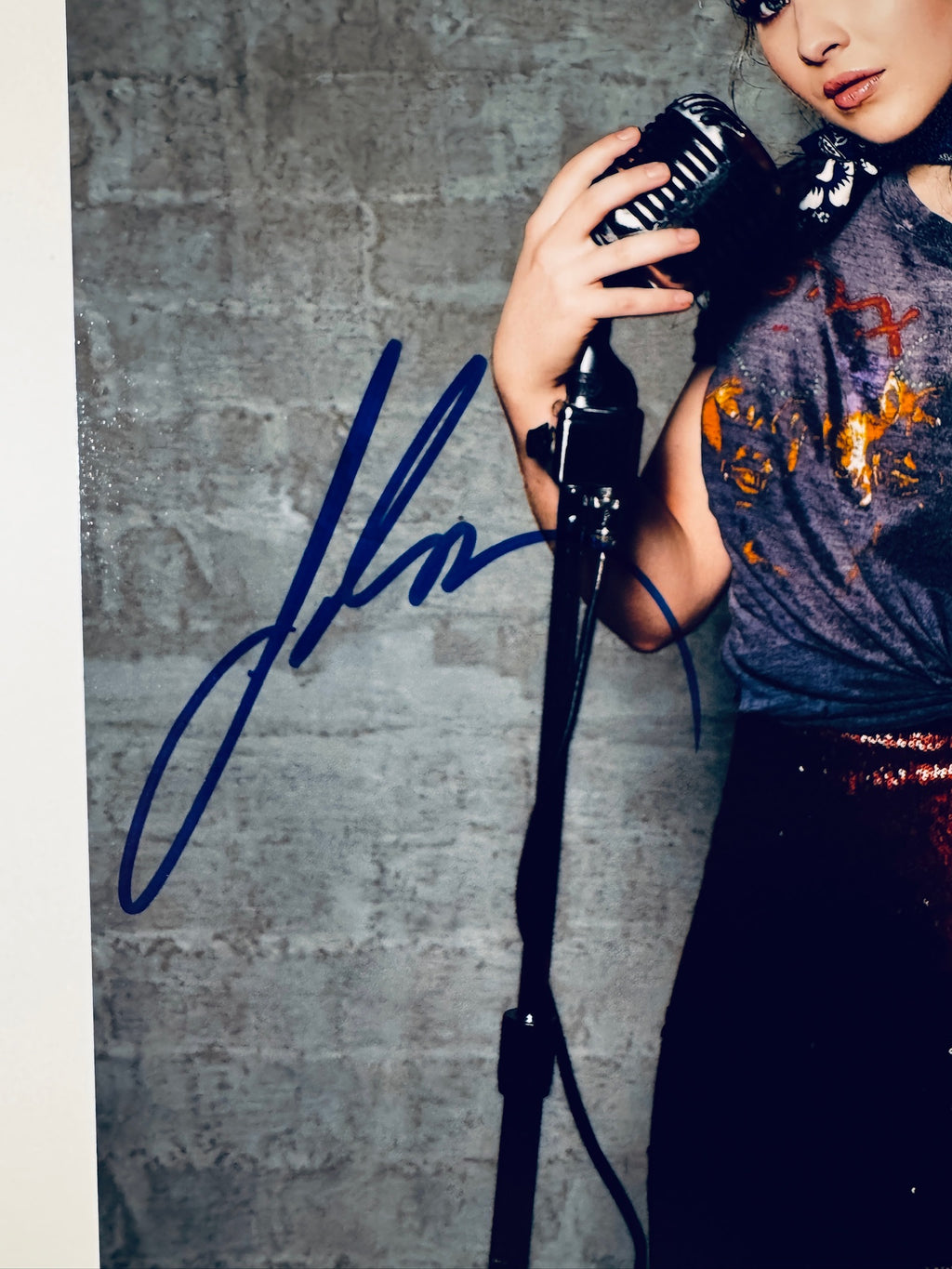 Close-up view of Sabrina Carpenter's blue autograph next to the microphone stand on the promotional photograph.