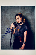 Signed full photo of Sabrina Carpenter holding a vintage microphone against a brick wall backdrop, featuring a blue autograph.