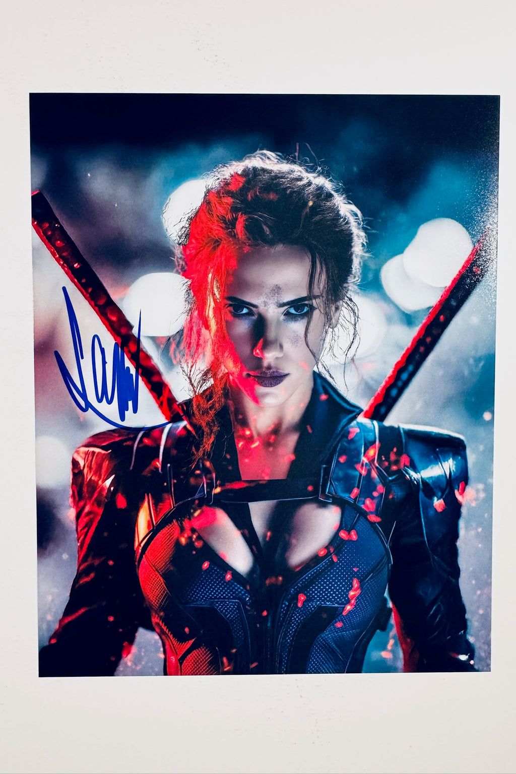 A close-up portrait of Scarlett Johansson as Natasha Romanoff with red-tinted hair and dark tactical armor against a blue-toned blurred background, featuring a blue marker signature across the left side.