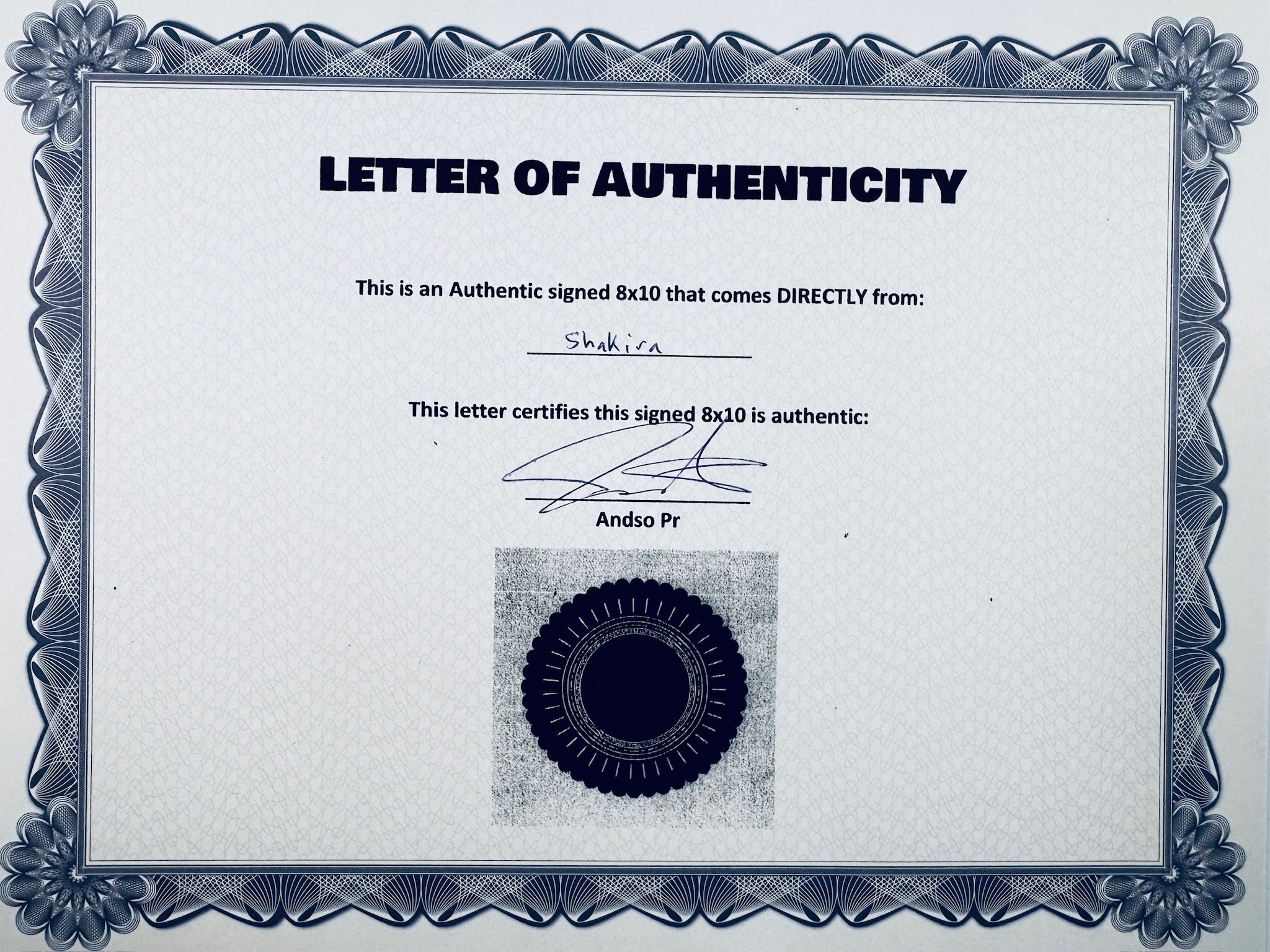 A Letter of Authenticity with a decorative blue-patterned border, certifying an authentic signed 8x10 coming directly from Shakira, featuring a dark circular seal graphic at the bottom.