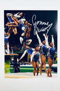A composite action photograph of Simone Biles competing in a blue and red leotard at the Olympics, showing multiple phases of her vault routine and standing poses, featuring a silver marker signature in the upper right.