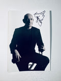 Full-shot autographed black and white photograph of actor Sir Ben Kingsley seated in a suit.