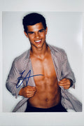 A portrait of Taylor Lautner smiling and wearing an open striped button-down shirt that exposes his torso, featuring a blue marker signature on the lower left.