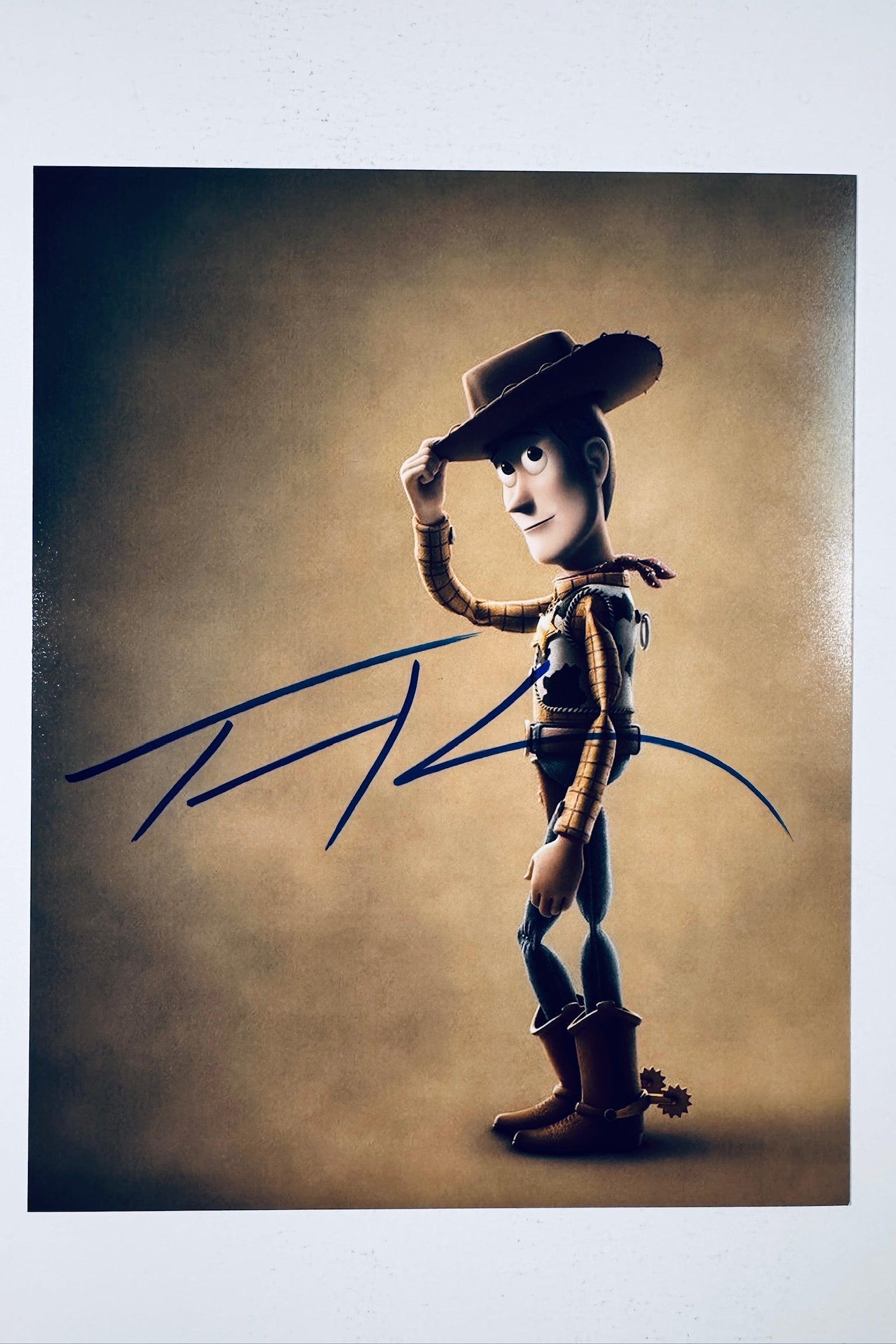 Signed full photo of Woody from Toy Story tipping his hat, featuring a blue autograph.