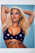 Signed 8x10 matte promotional photo of WWE Hall of Famer Trish Stratus posing in a black bikini top with buttons against a light blue background, featuring a bold black ink autograph.