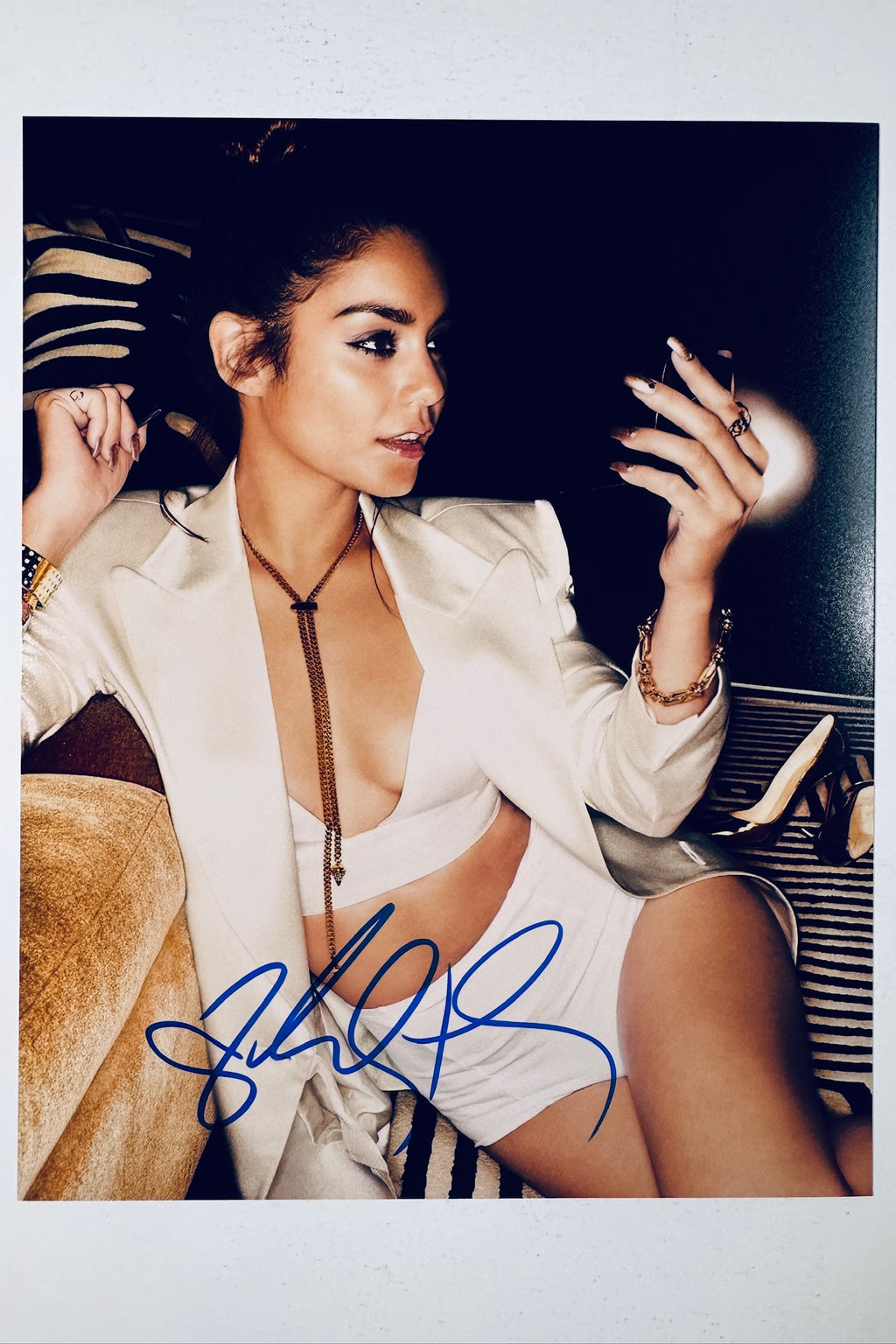 Signed full photo of Vanessa Hudgens posing in a white outfit and blazer holding a compact mirror, featuring a blue autograph.