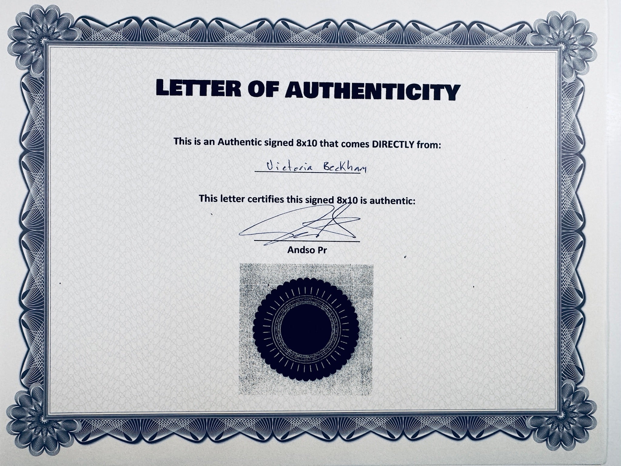 A Letter of Authenticity with a decorative blue-patterned border, certifying an authentic signed 8x10 coming directly from Victoria Beckham, featuring a signature and a dark circular seal graphic at the bottom.