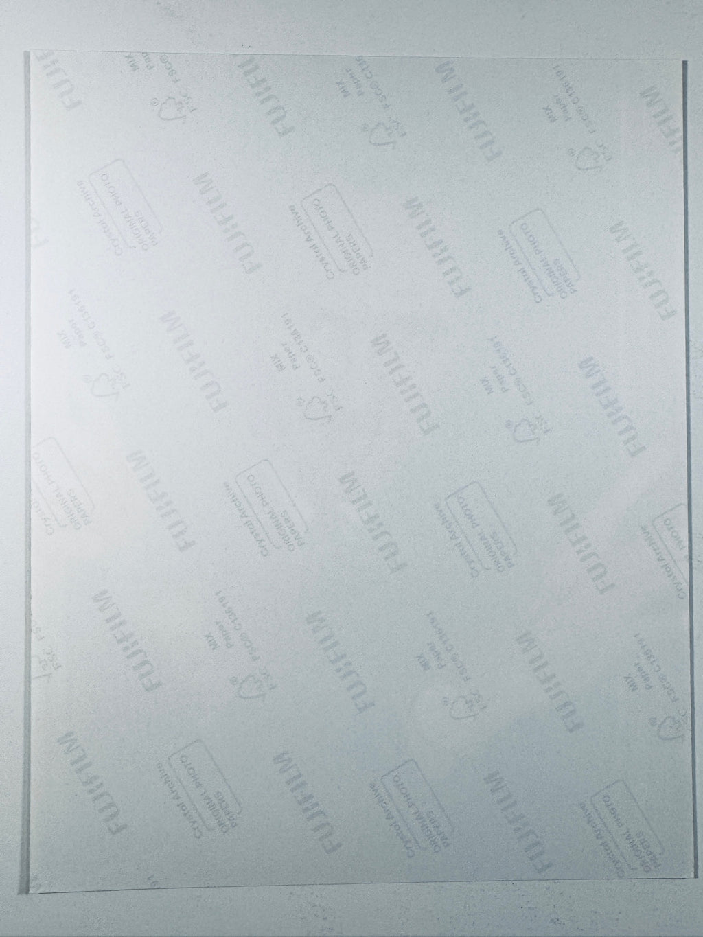 The plain white reverse side of a photographic print showing faint translucent watermark patterns and repeating Fujifilm paper logos.