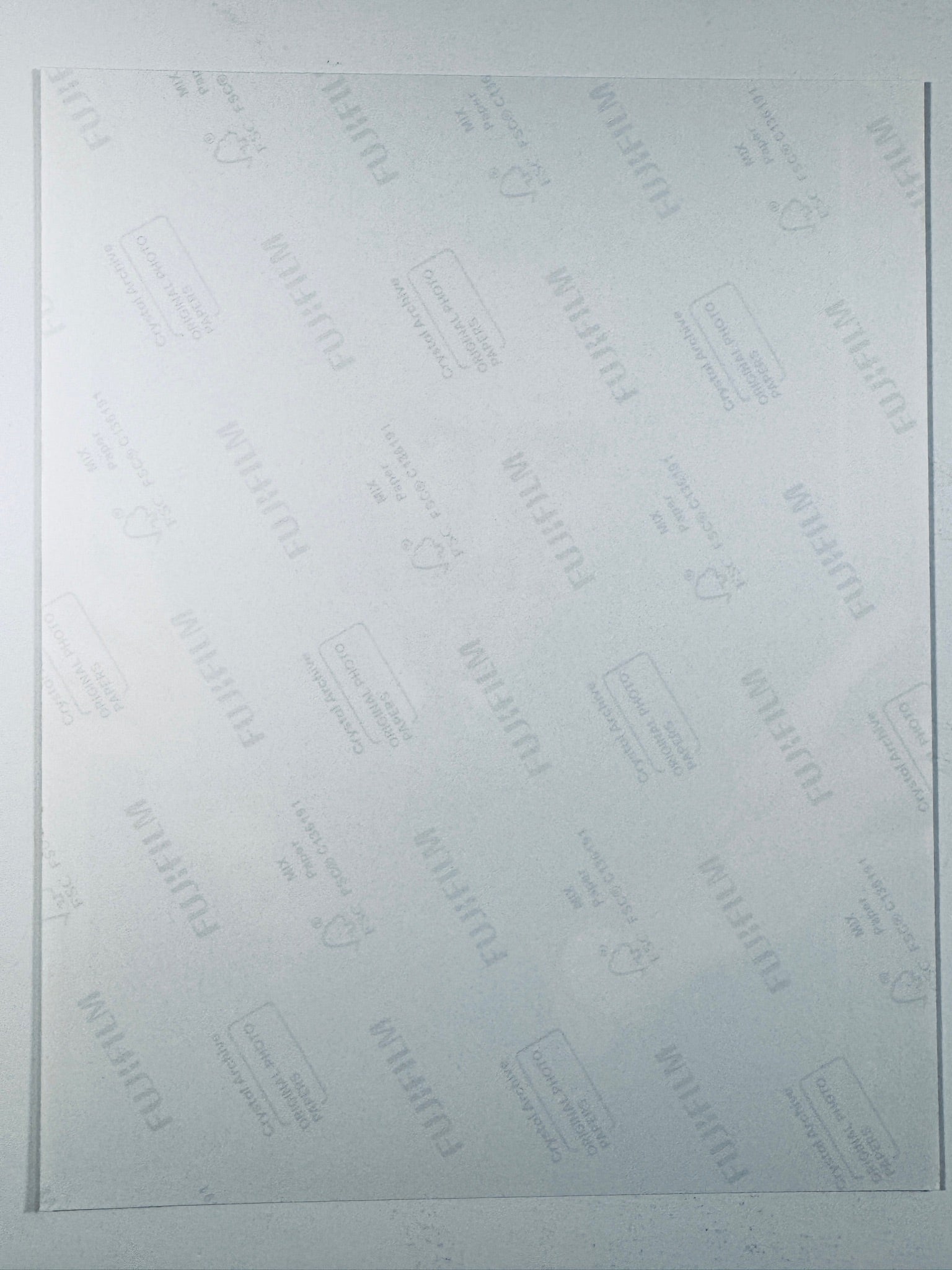 The plain white reverse side of a photographic print showing faint translucent watermark patterns and repeating Fujifilm paper logos.
