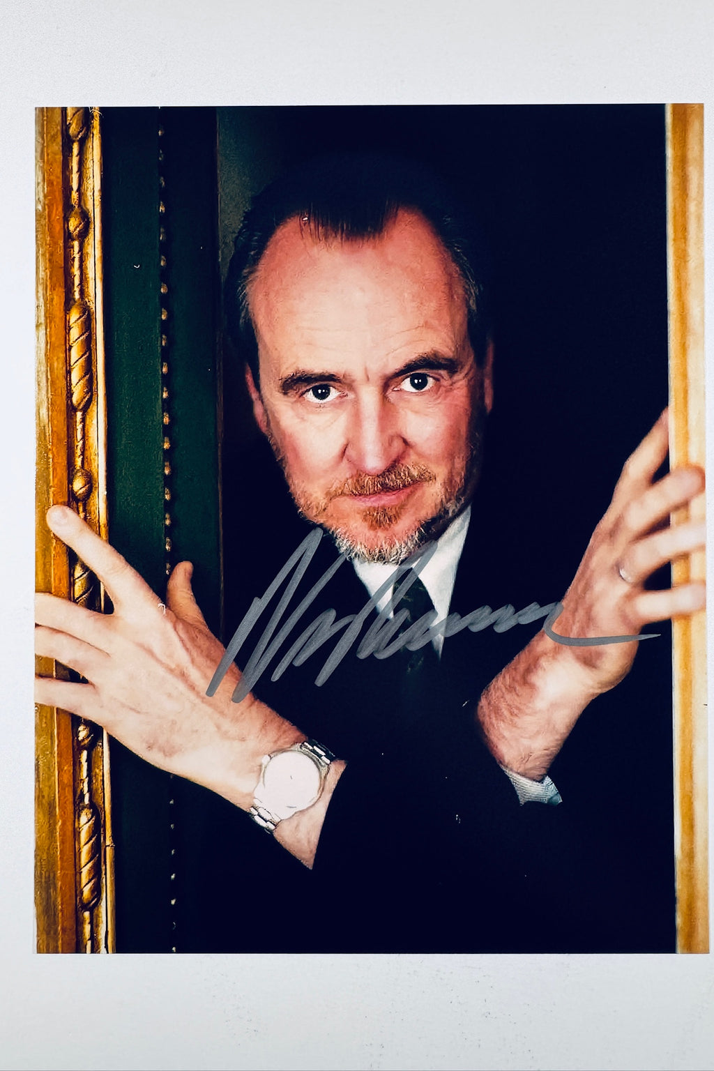 A portrait of filmmaker Wes Craven posing between a door frame with hands raised, featuring a bold signature across his chest.