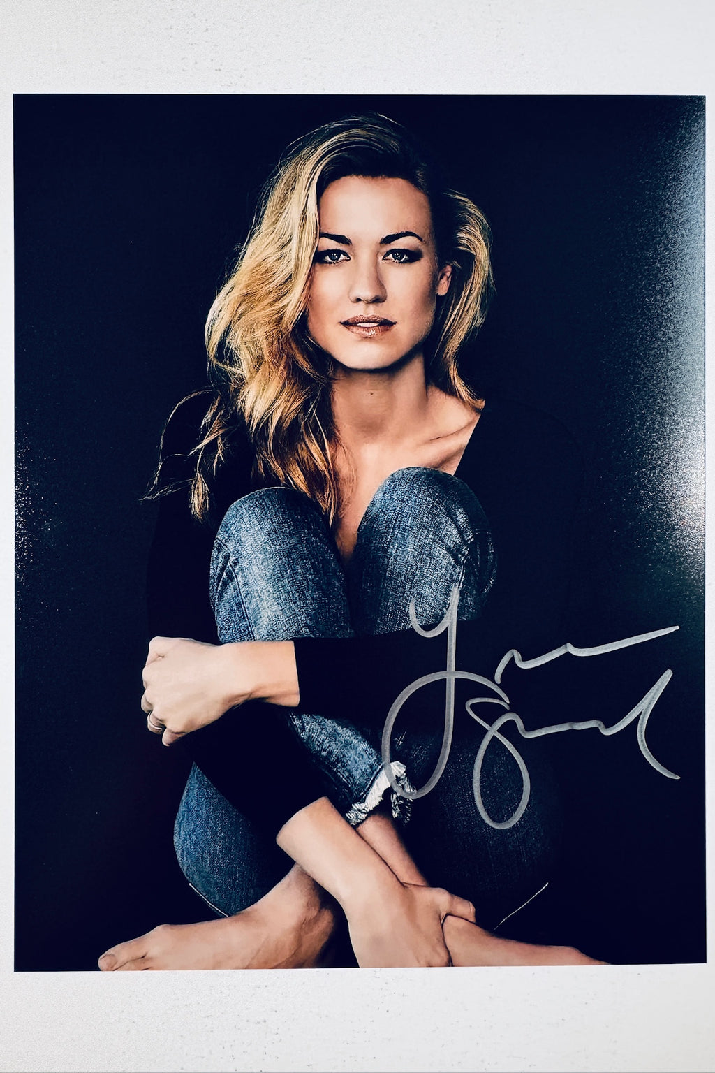 Signed 8x10 matte promotional photo of actress Yvonne Strahovski sitting with jeans and a black top against a dark background, featuring a bold silver ink autograph.